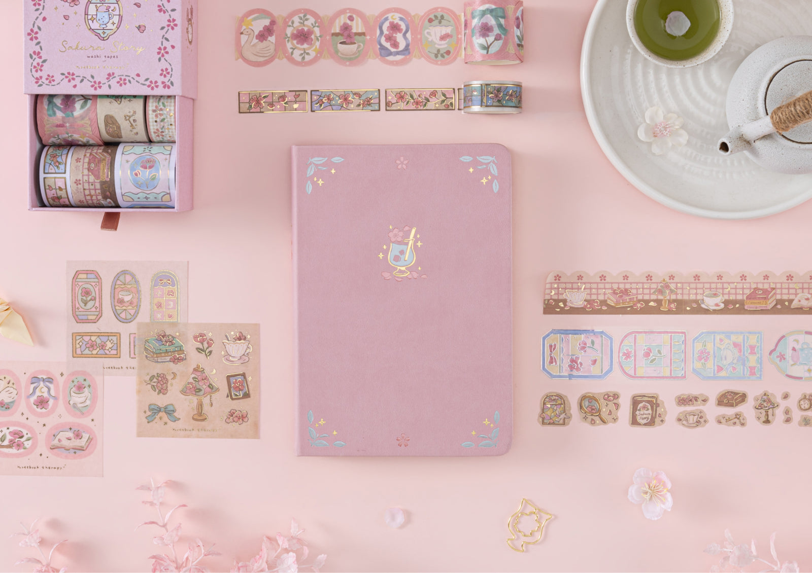 The Matcha Blossom pink notebook and Tsuki Sakura Story Washi Tape Set placed on a pink background.