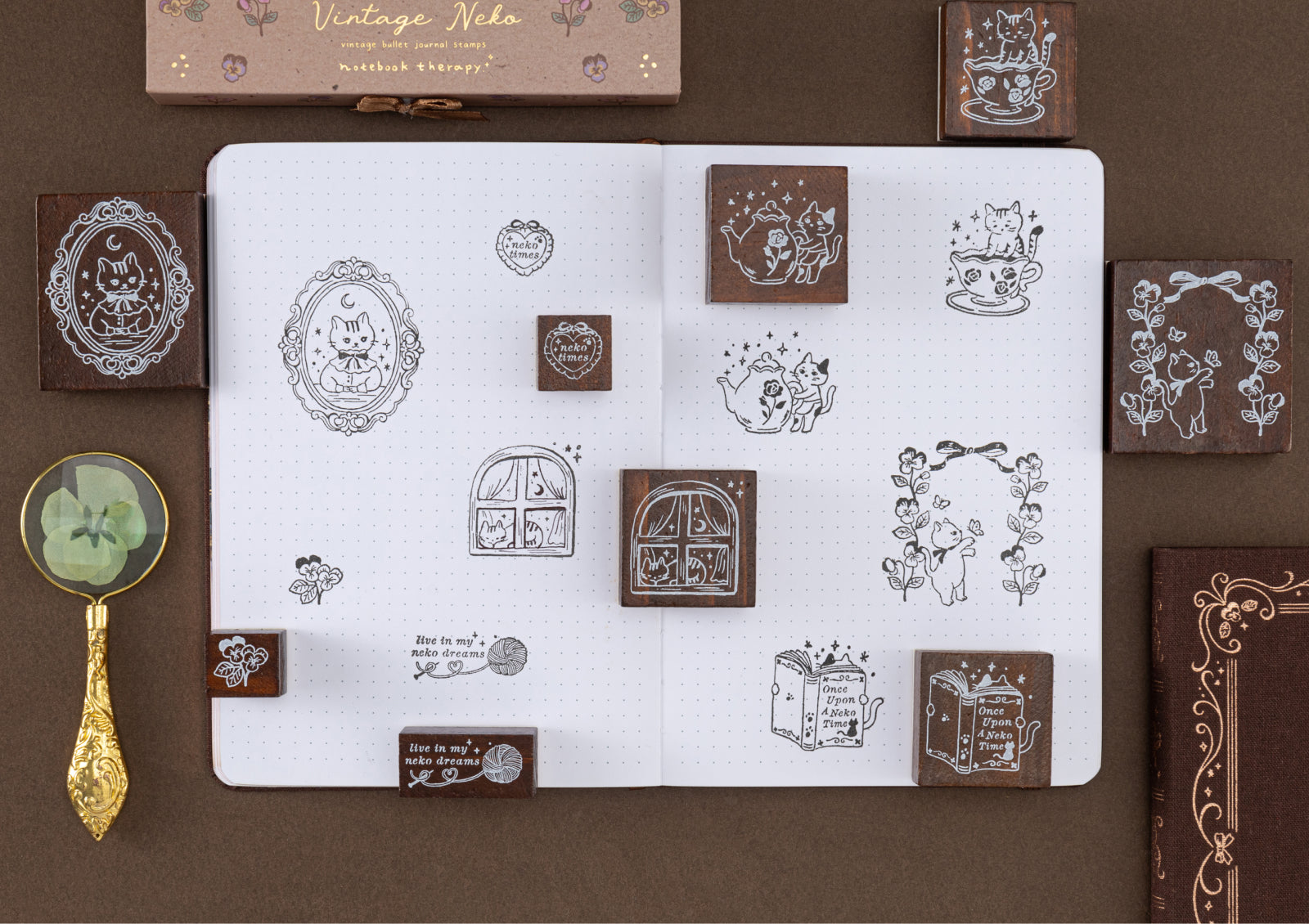 Top-down view of an open dotted journal featuring multiple vintage-style cat stamp designs and the wooden stamps used to create them.