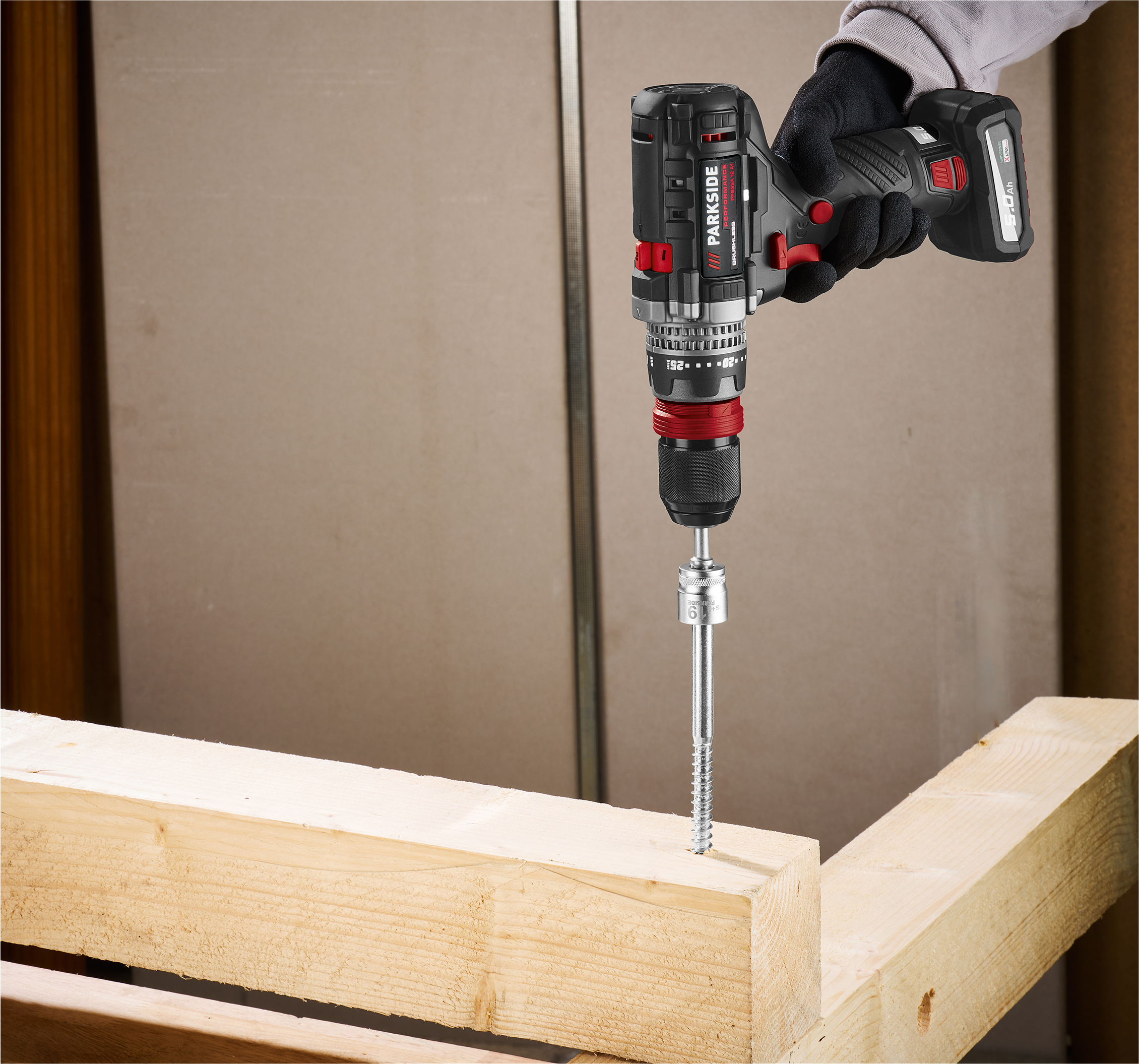 Une visseuse-perceuse sans fil Parkside Performance visse une vis dans une poutre en bois.