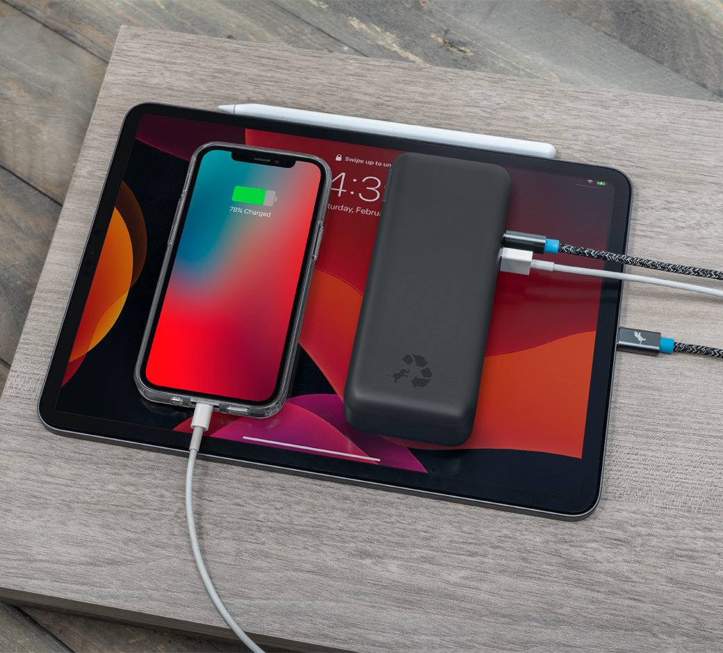 Power bank charging a smartphone and tablet, connected via multiple cables on a table.