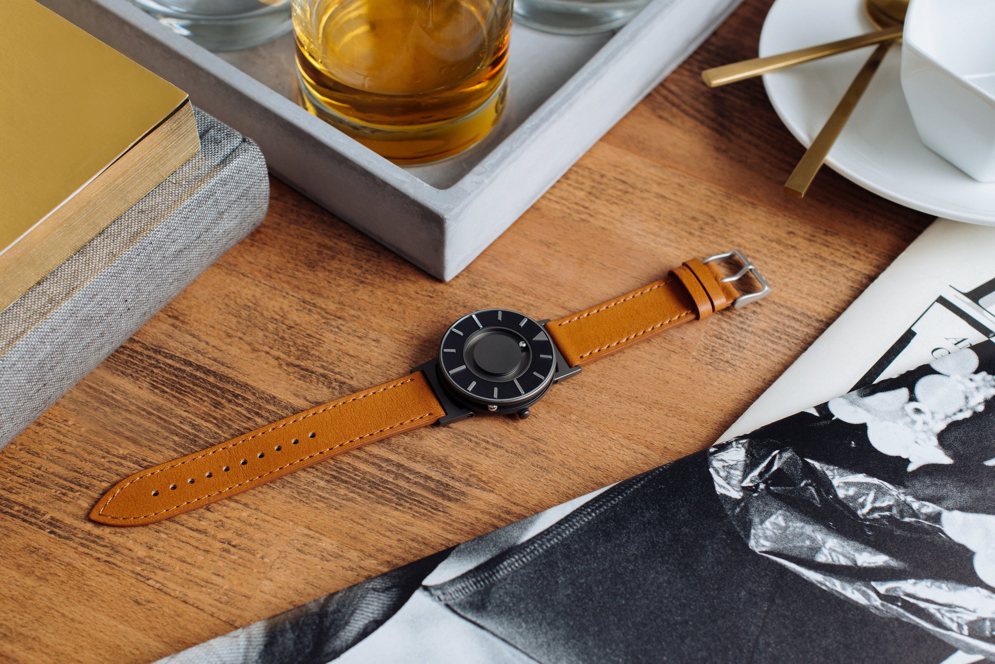 The Bradley Voyager Cobalt is flat on a wood table. There is a white tray with a drink in the background.