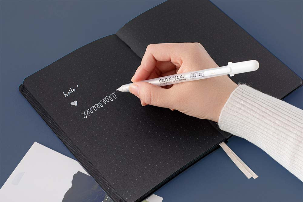 Open Tsuki Black Paper Limited Edition Hardcover Bullet Journal with Gelly Roll Pen held in hand in navy background