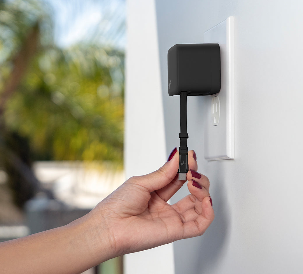 Hand with red nail polish pulling USB-C cable down from Black Wall Charger. Window with palm tree blurred in background