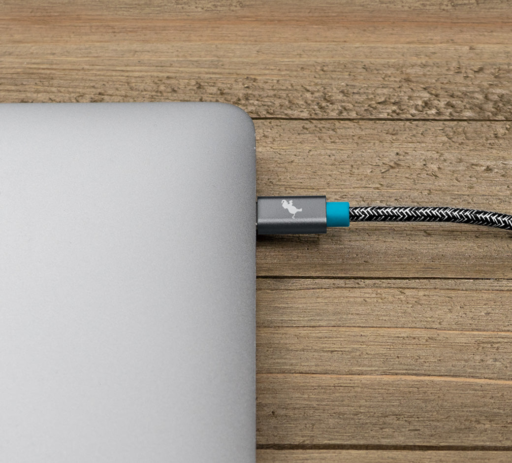 USB-C charging cable plugged into a laptop on a wooden surface.