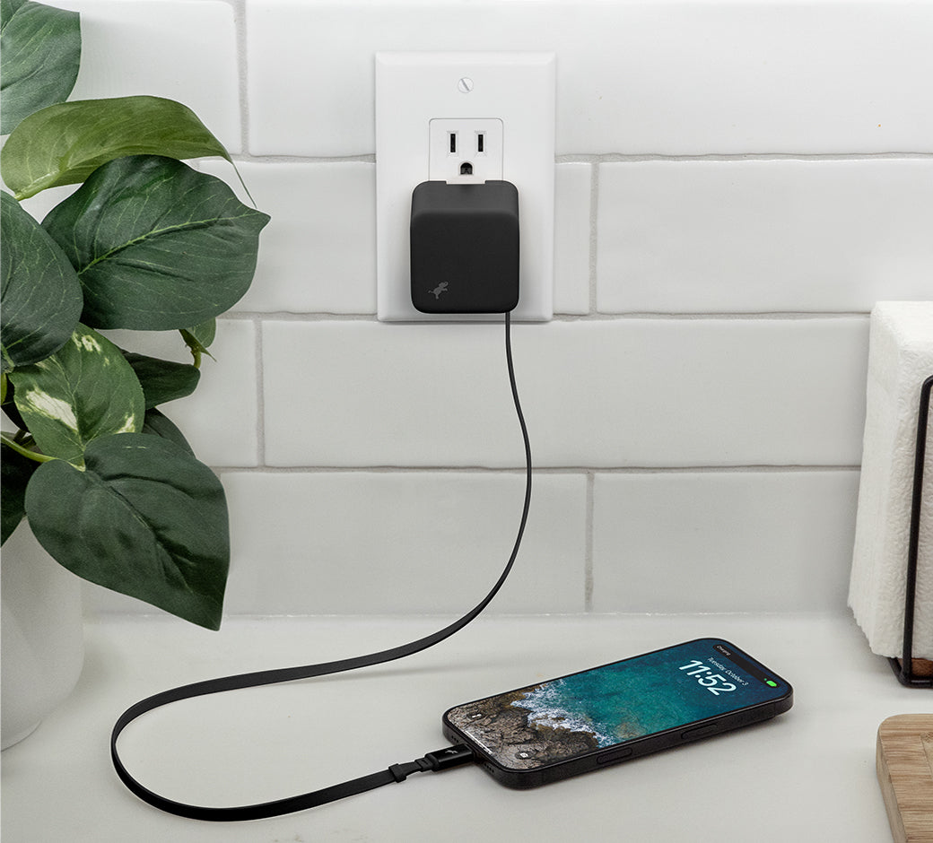 Black wall charger with USB-C cable connected to iPhone on white quartz kitchen counter.