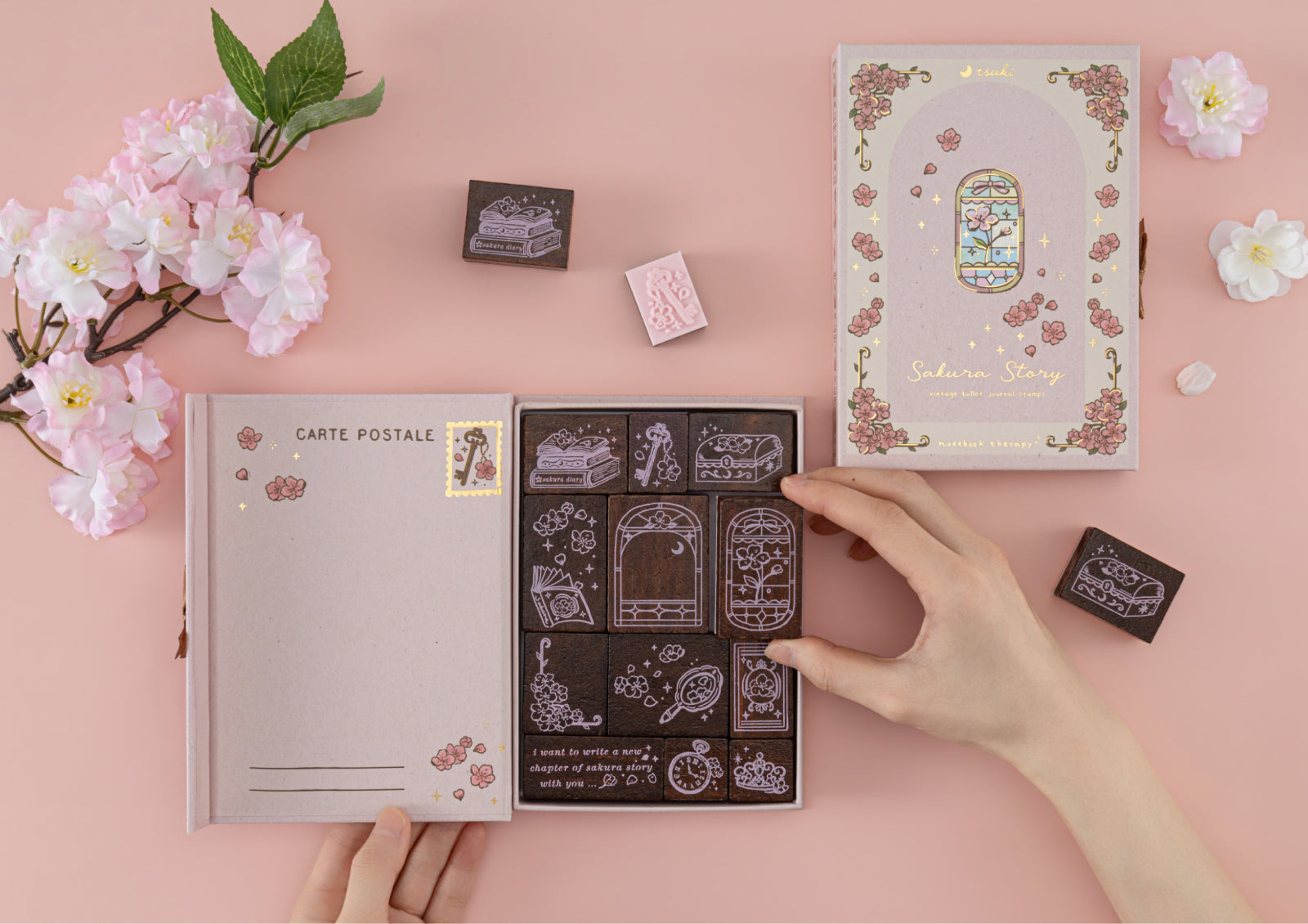 A hand picking a wooden stamp from the collection box featuring various floral and vintage window designs.