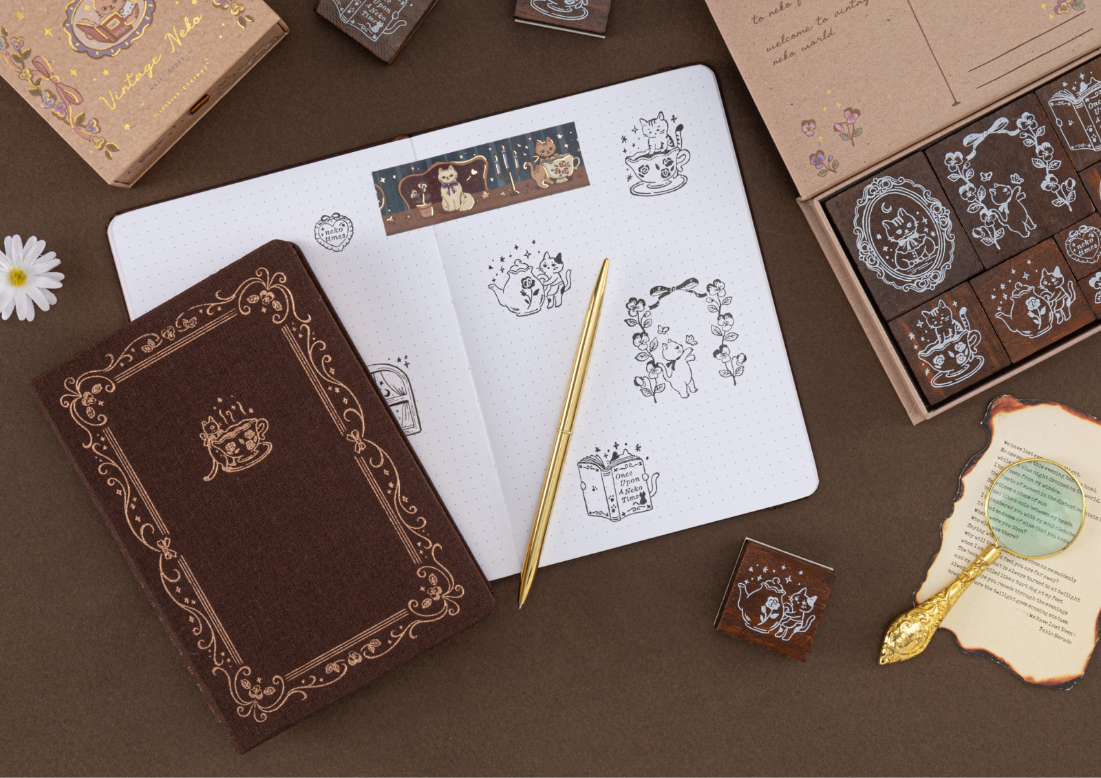 A flat lay featuring a brown fabric journal, a gold pen, and the Vintage Neko stamp set with several stamped cat illustrations in a notebook.