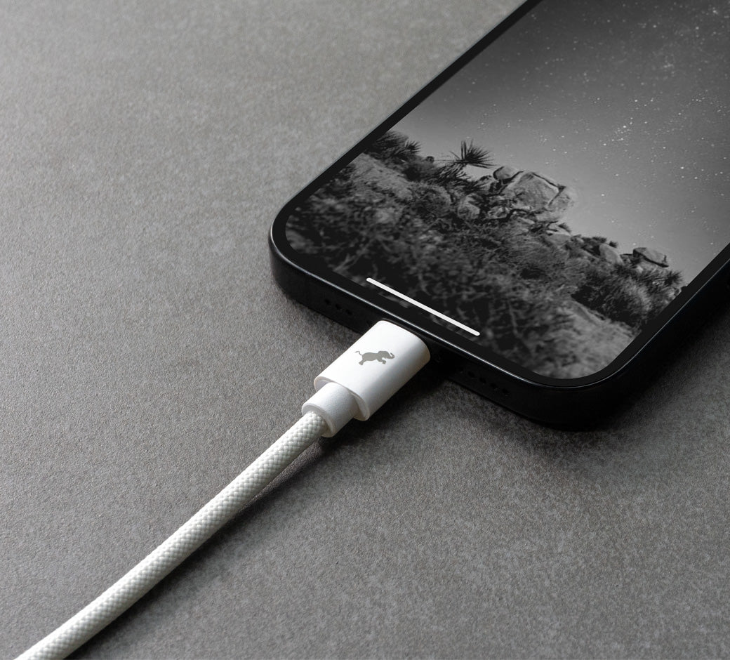 Close up of a white cable connected to iPhone on dark slate surface.