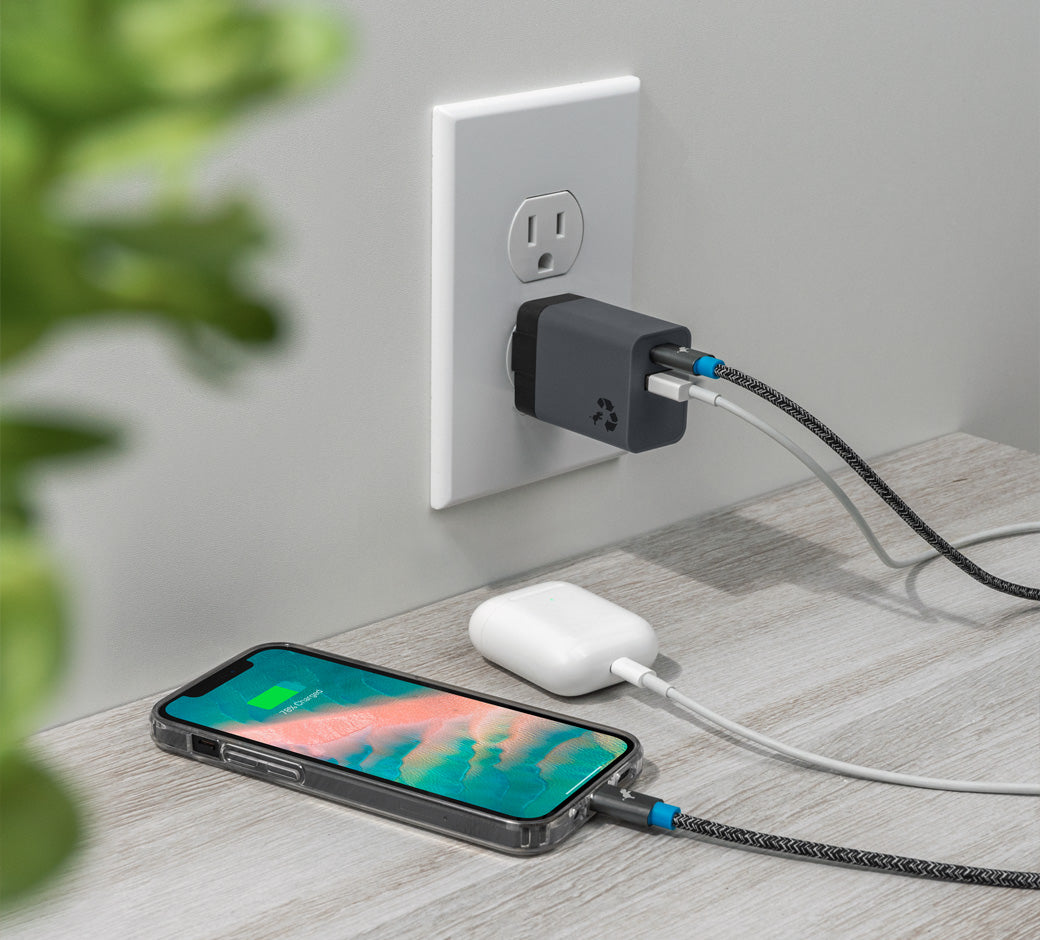 USB wall charger plugged into an outlet, charging a phone and AirPods on a table.