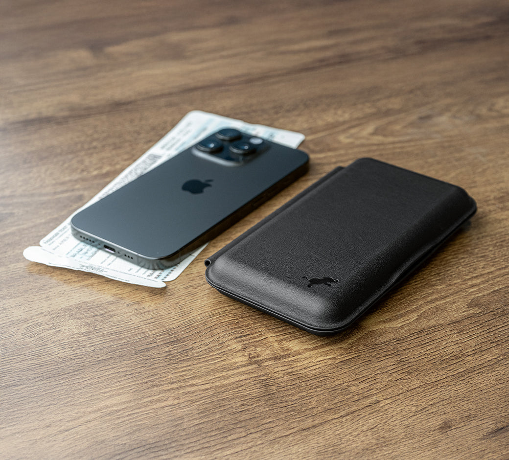 A phone and a black wallet case placed on a wooden surface with some bills next to them.