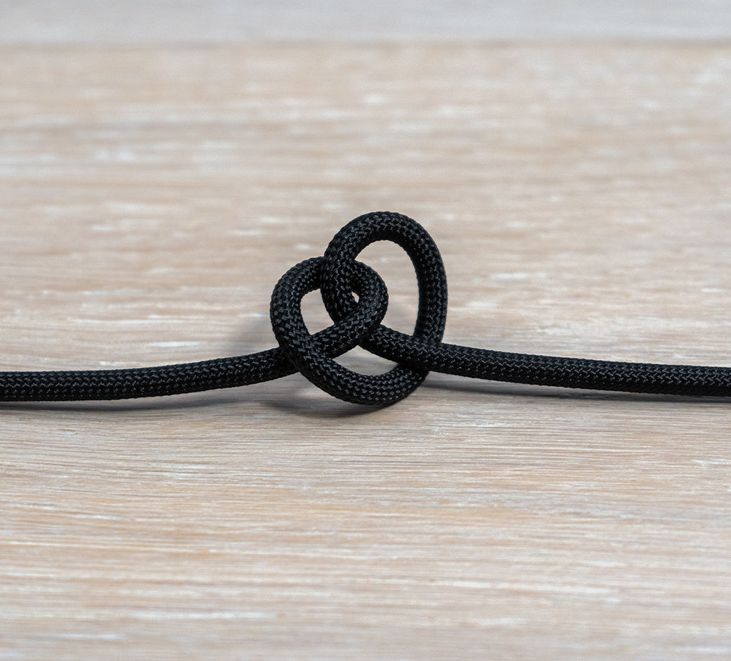 Black braided USB-C cable tied in a knot on a wooden surface.