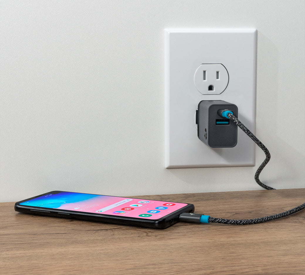 Smartphone connected to a USB-C wall charger via a braided cable, placed on a wooden surface.