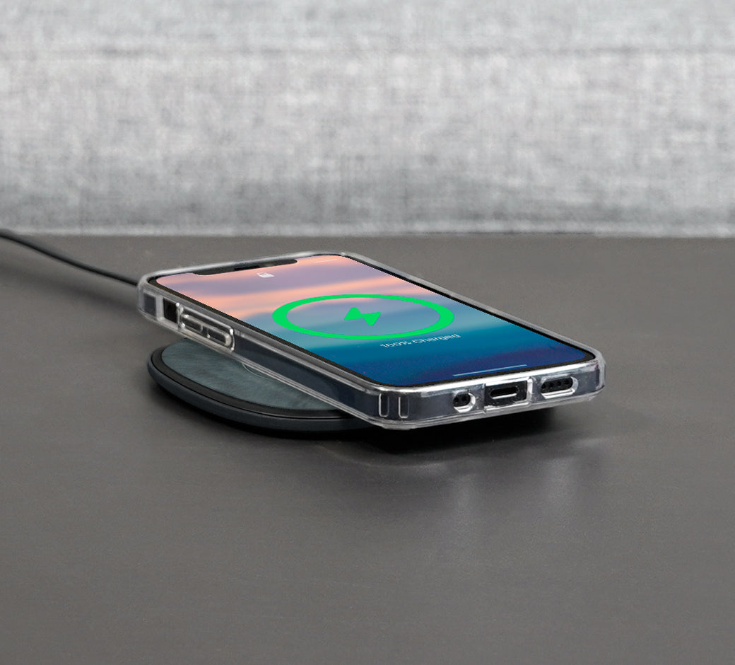 Smartphone on a compact wireless charger on a dark surface, displaying charging status.