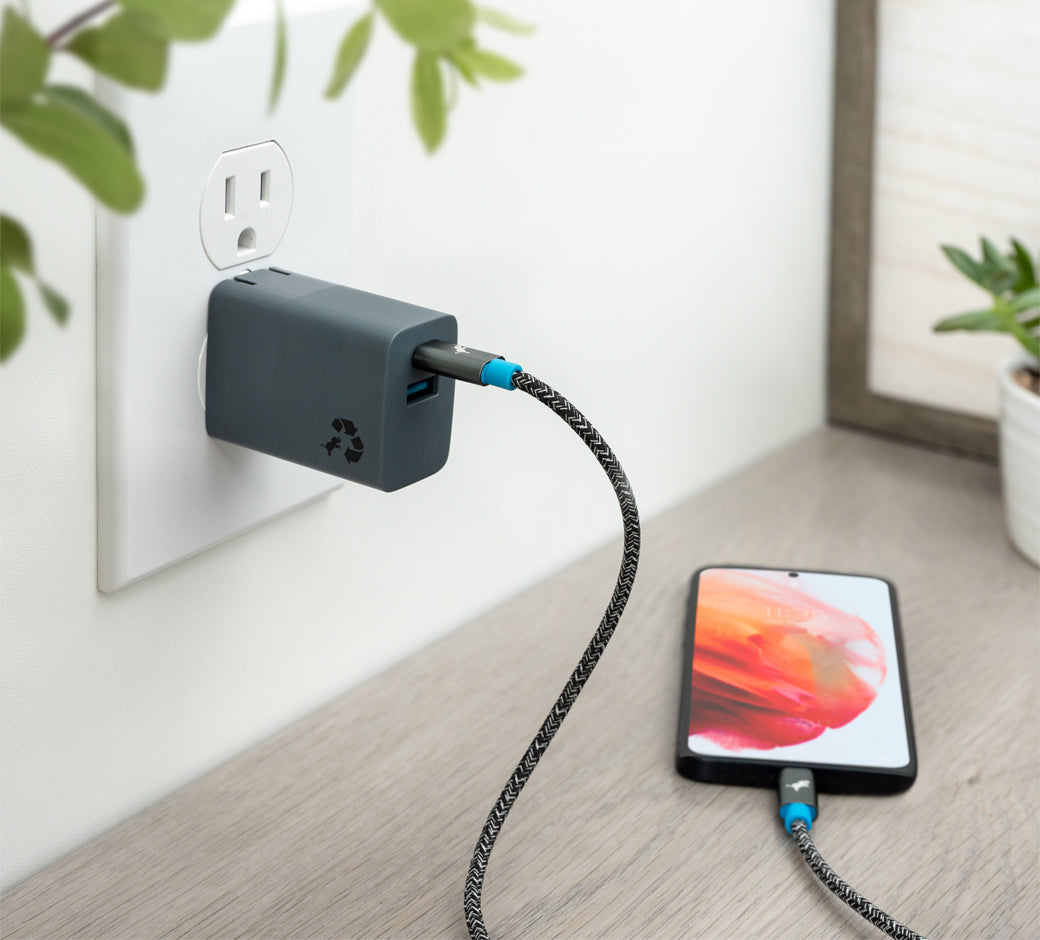 Wall charger connected to a phone placed on a table, surrounded by green plants.