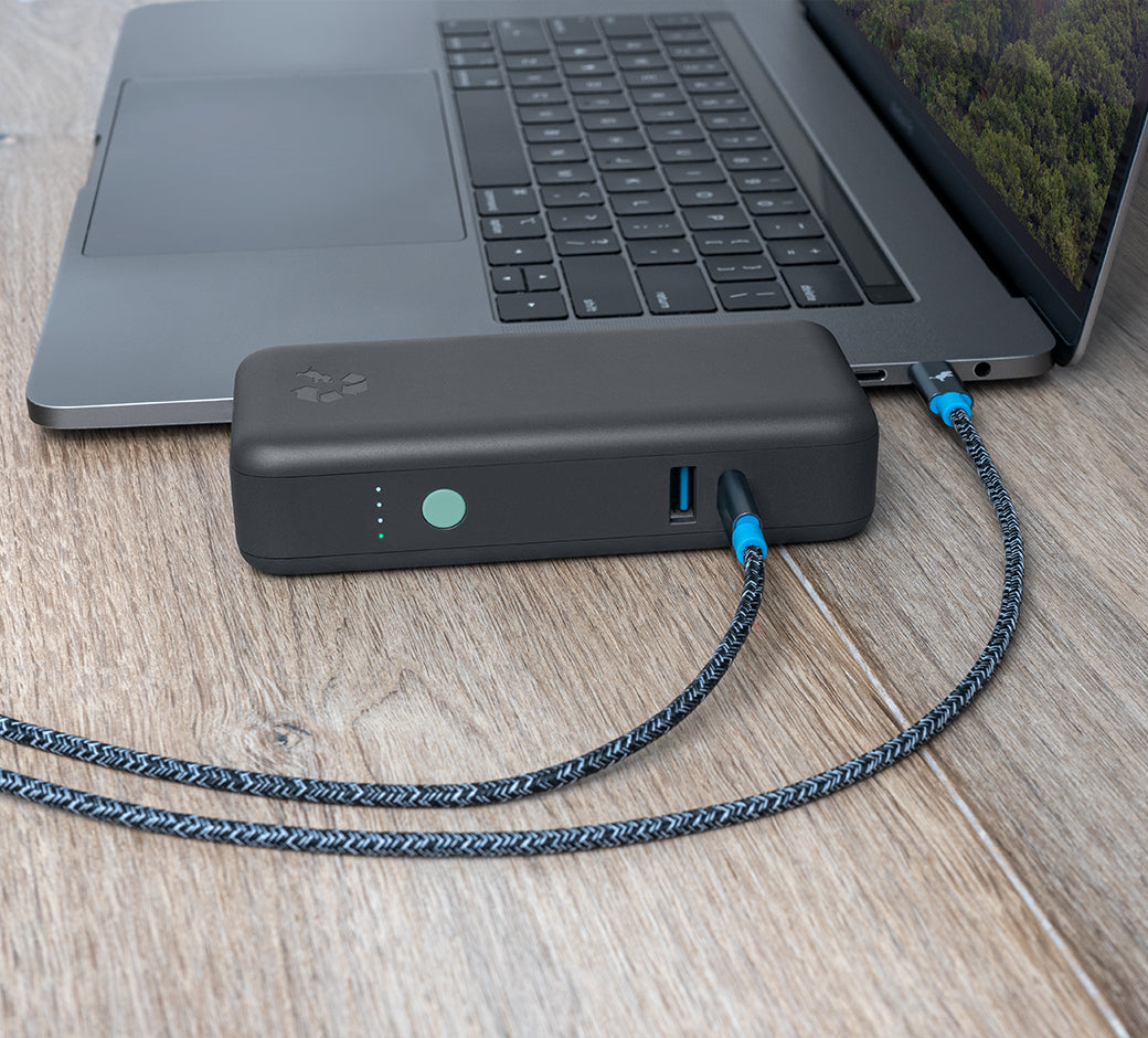 Portable power bank plugged into a wall outlet charging a smartphone and laptop.