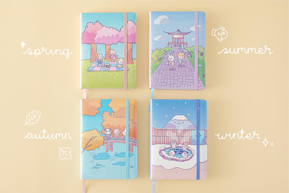 Tsuki ‘Four Seasons: Autumn Edition’ Bullet Journal made with milkkoyo held in hand with Tsuki ‘Four Seasons: Summer Edition’ notebook and Tsuki ‘Four Seasons: Spring Edition’ bujo and Tsuki ‘Four Seasons: Winter Edition’ bullet journal on light brown background