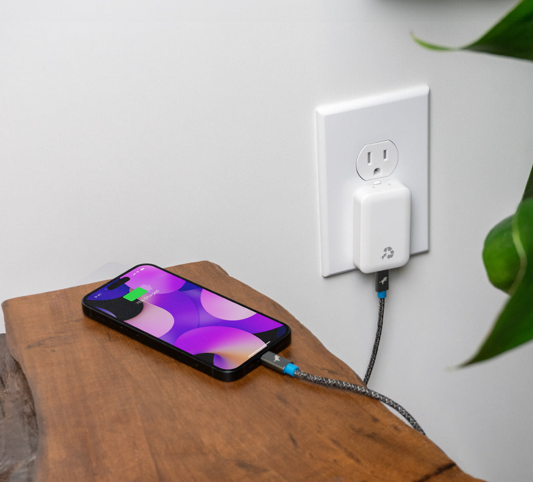 Smartphone charging on a wooden surface via a slim wall charger.