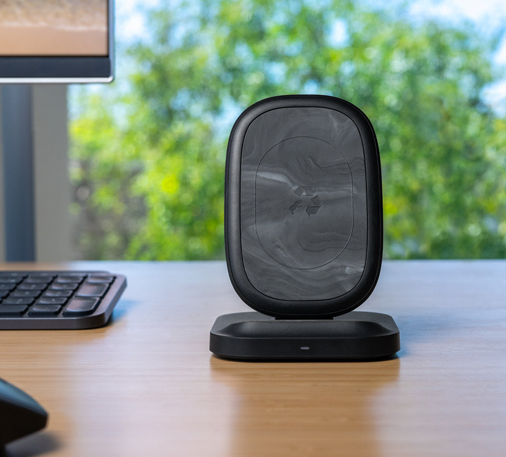 Black wireless charging stand with a marbled design, placed on a desk near a keyboard.
