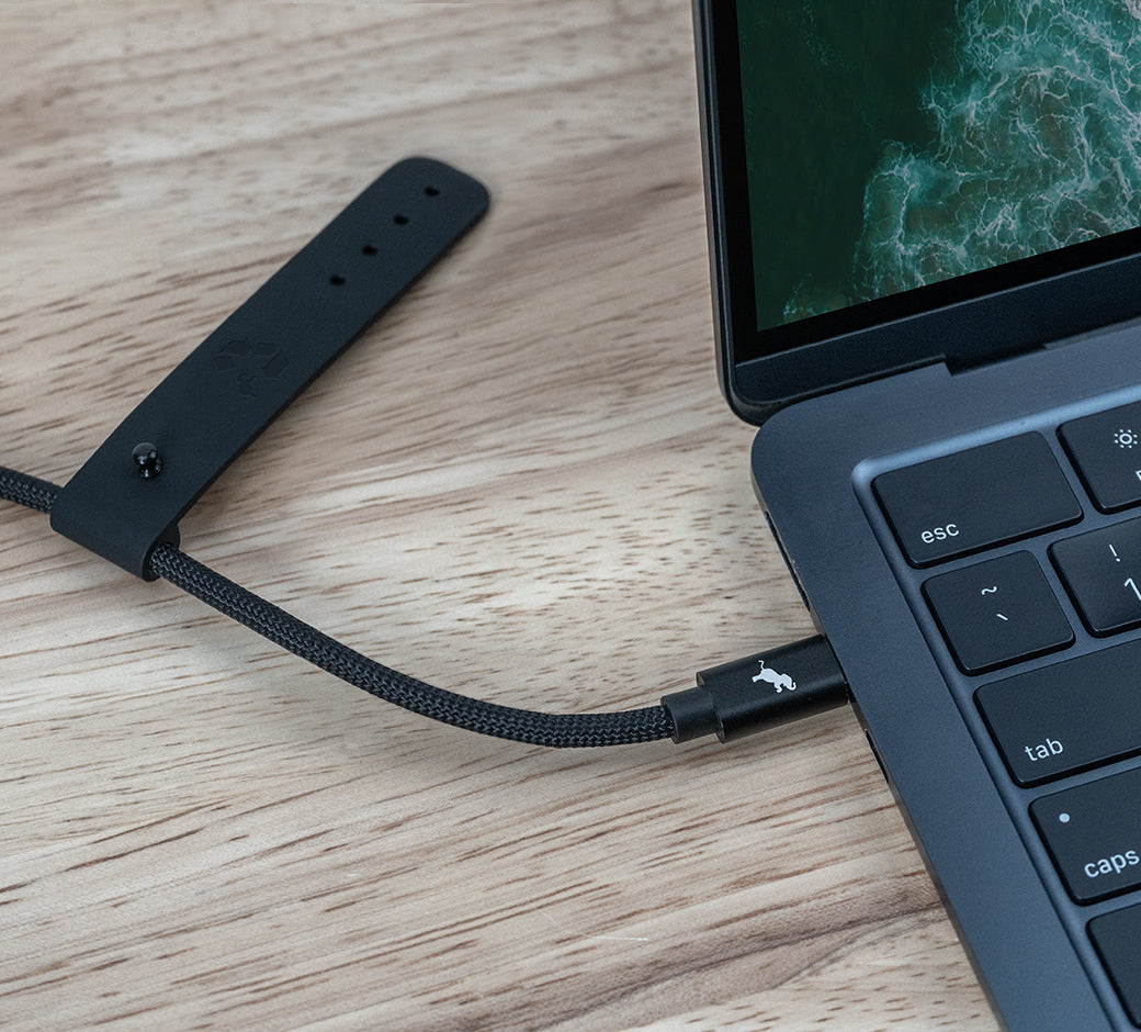 USB-C cable connected to a laptop with a black leather strap holding the cable.