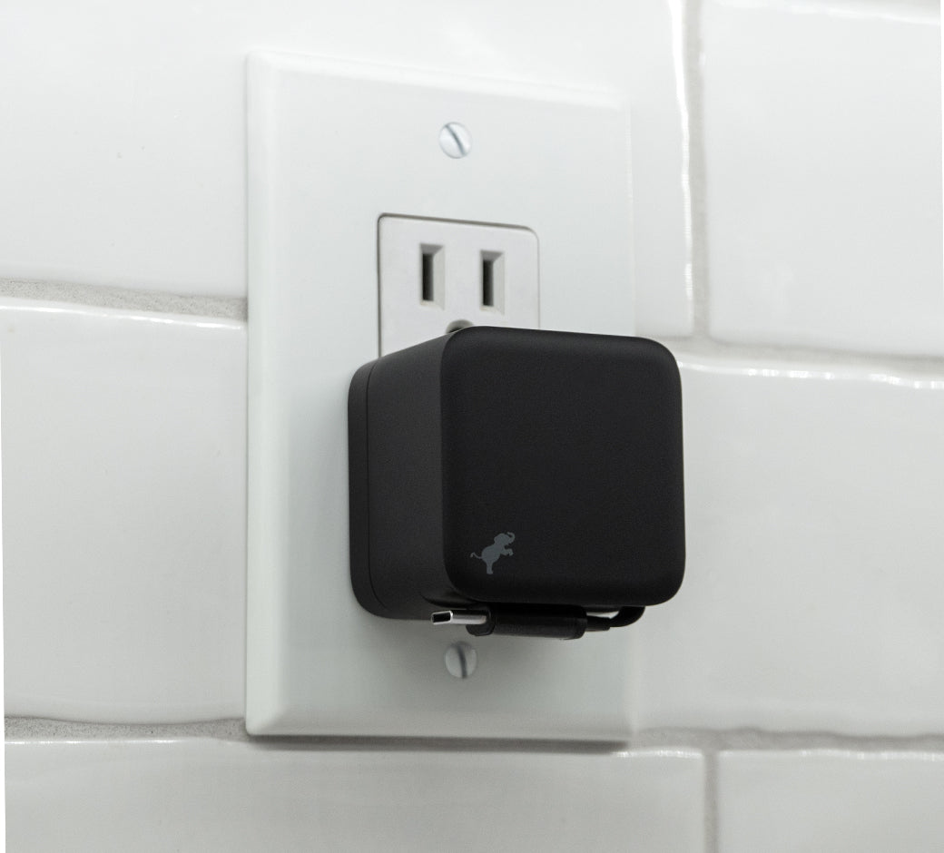 Black wall charger plugged into a white tiled wall, with the cable neatly retracted and stored at the bottom.