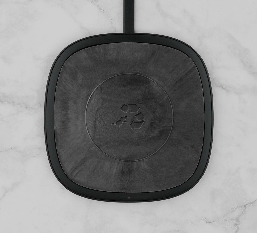 Square black wireless charging pad with a marbled design and recycling logo on a marble surface.