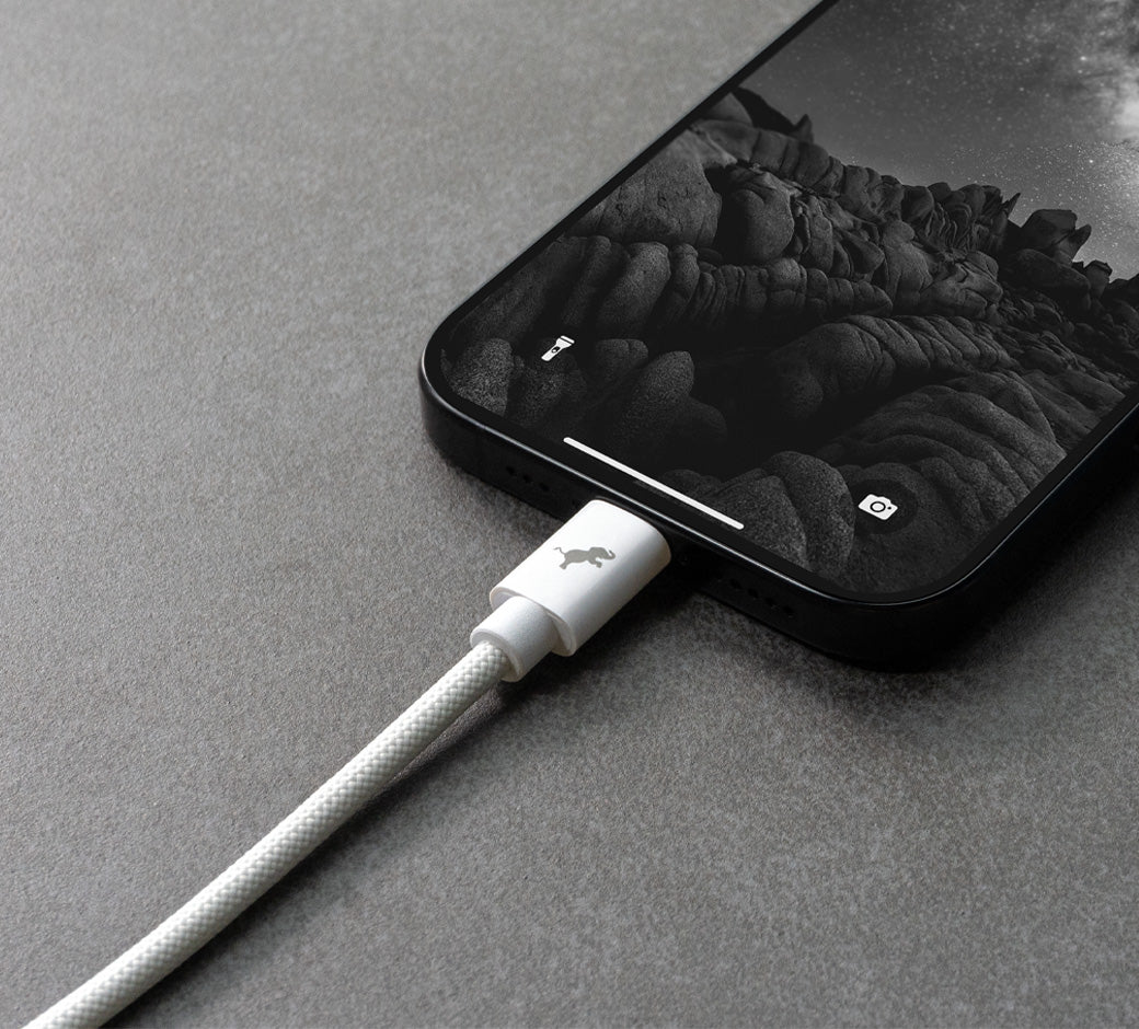 Close up of a white cable connected to iPhone on dark slate surface.
