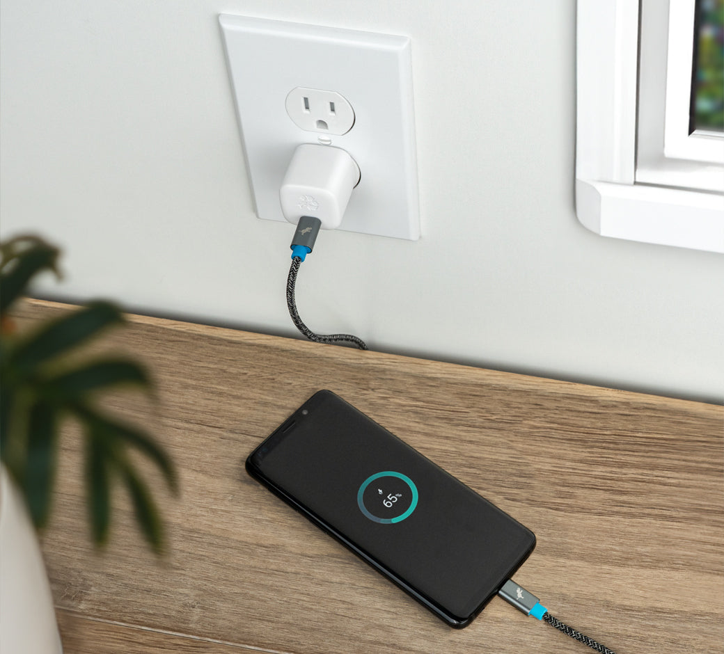 White 30W USB-C wall charger plugged into an outlet charging a smartphone on a wooden table.