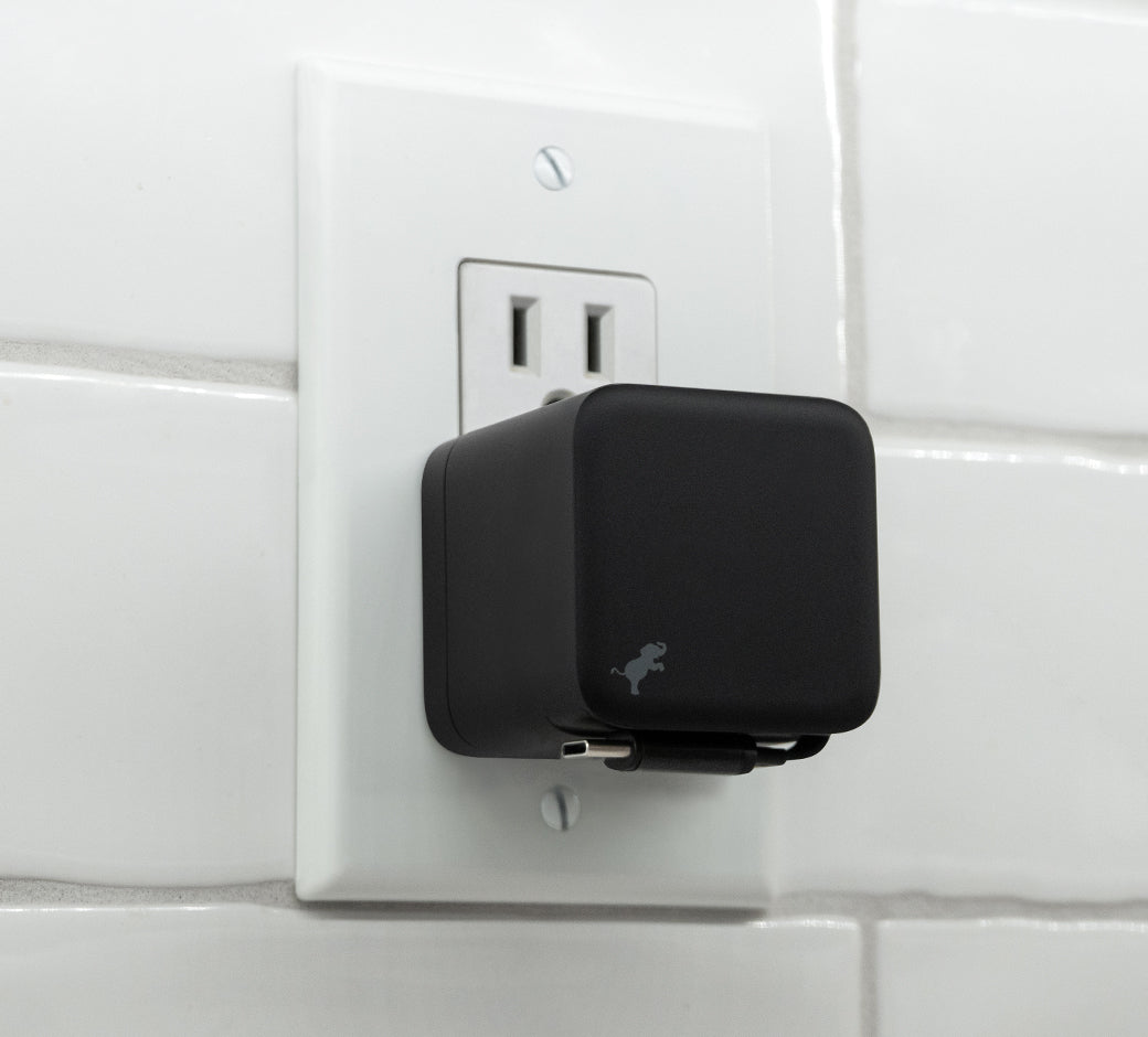 Black wall charger plugged into a white tiled wall, with the cable neatly retracted and stored at the bottom.