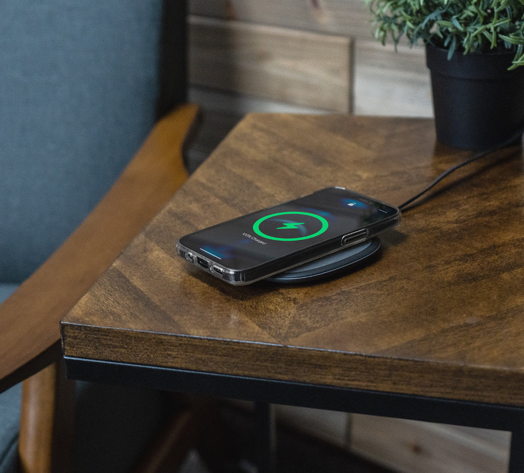 Phone charging on a sleek black pad on a wooden side table beside a chair and plant.