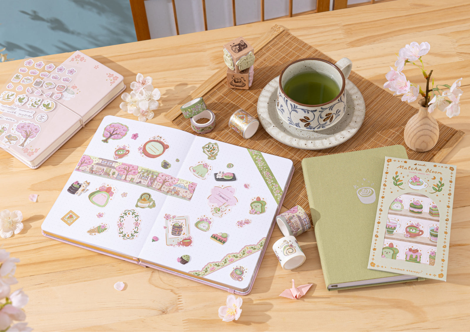 An open Matcha Bloom notebook decorated with themed stickers and washi tape next to a cup of green tea.