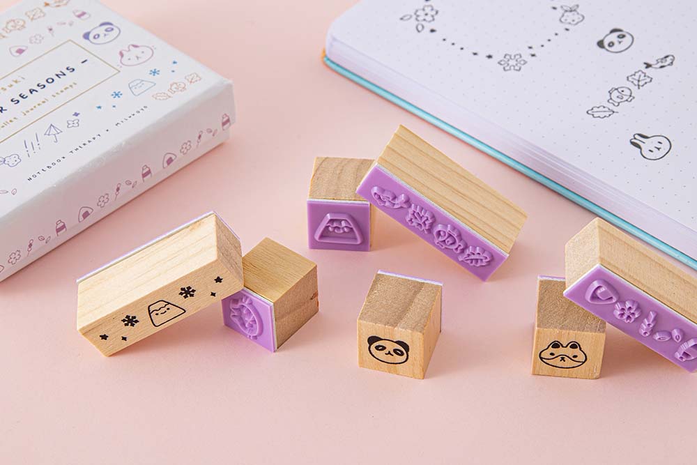 Close up of Tsuki ‘Four Seasons’ Bullet Journal Stamps by Notebook Therapy x Milkkoyo near open bullet journal on petal pink background