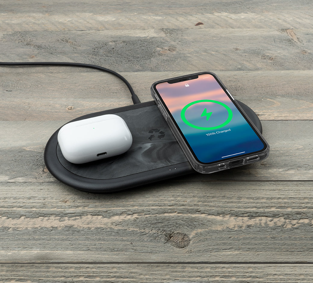 Charging pad on a wooden table with a phone (100%) and AirPods.