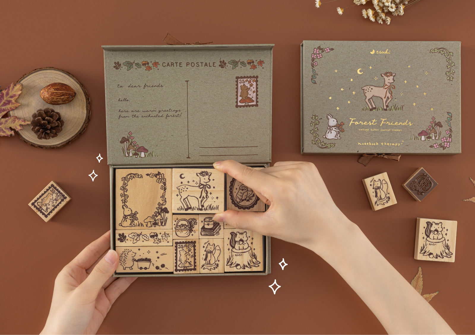 Hands holding open Forest Friends wooden stamp box, showing stamp blocks with whimsical animal and seasonal motifs.