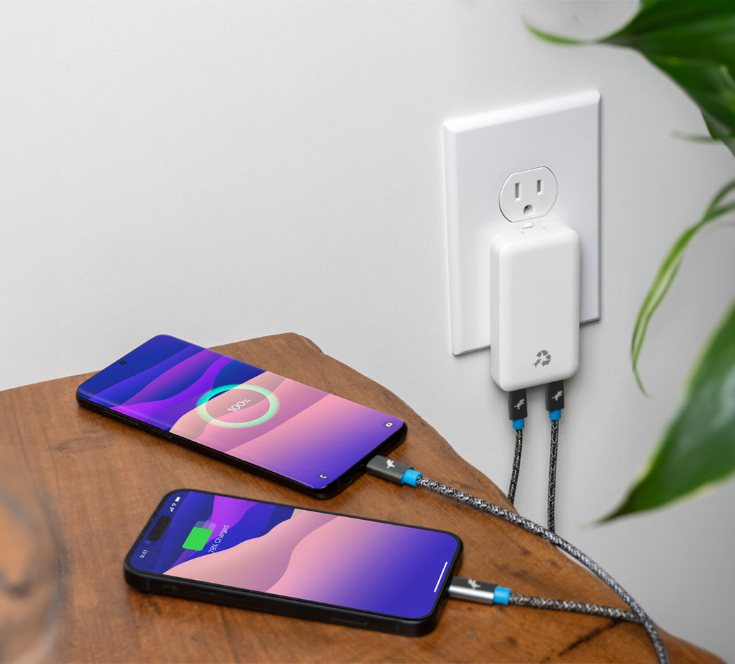 Two phones charging simultaneously via a white dual-port charger on a wooden surface.