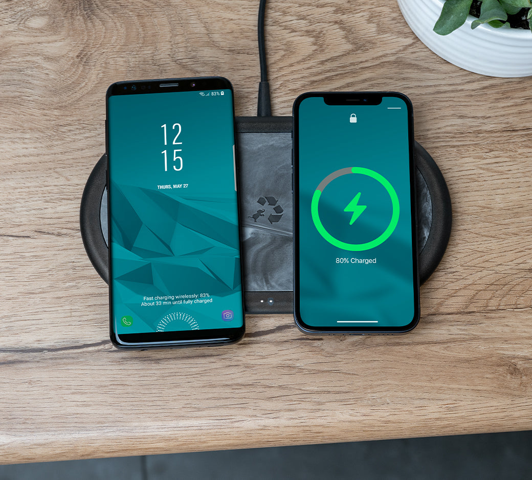 A wireless charging pad on a wooden surface charging an Android phone and an iPhone, both showing their charging status.