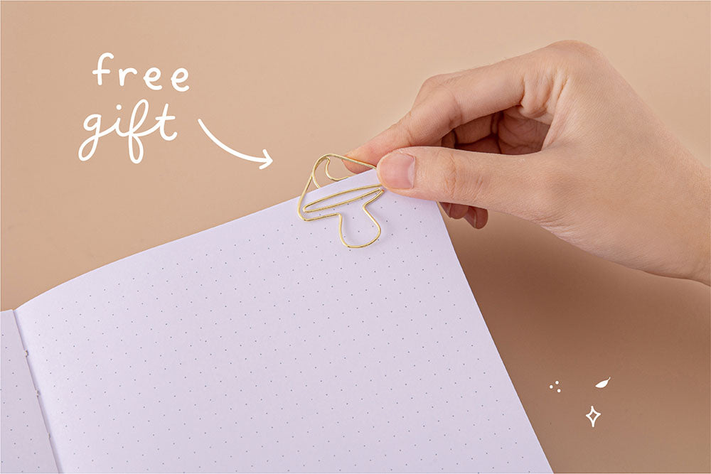 Open page of Tsuki ‘Kinoko’ Limited Edition Bullet Journal with free paperclip gift held in hand on beige background