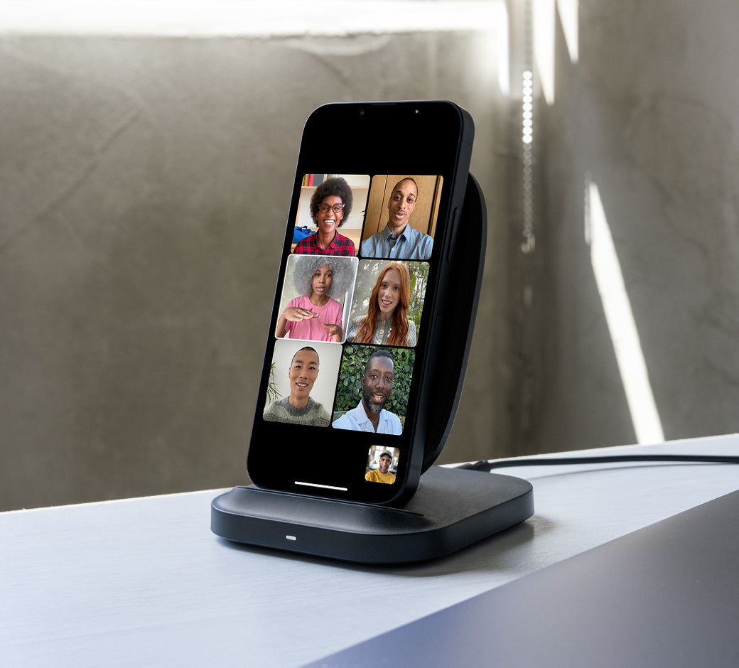 Smartphone on a wireless stand showing a video call with multiple participants in a well-lit room.