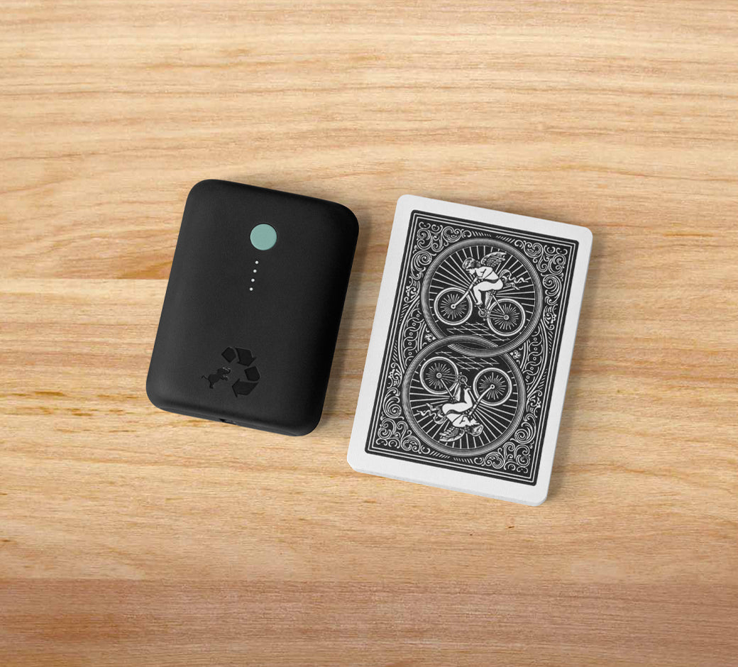 Compact black power bank with a recycling logo next to a deck of cards on a wooden surface.