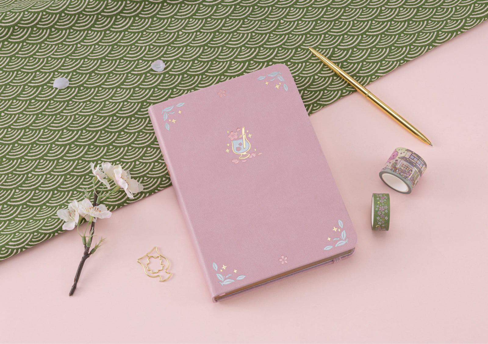The pink vegan leather Matcha Blossom notebook on a green seigaiha patterned cloth with a gold pen and washi tape.