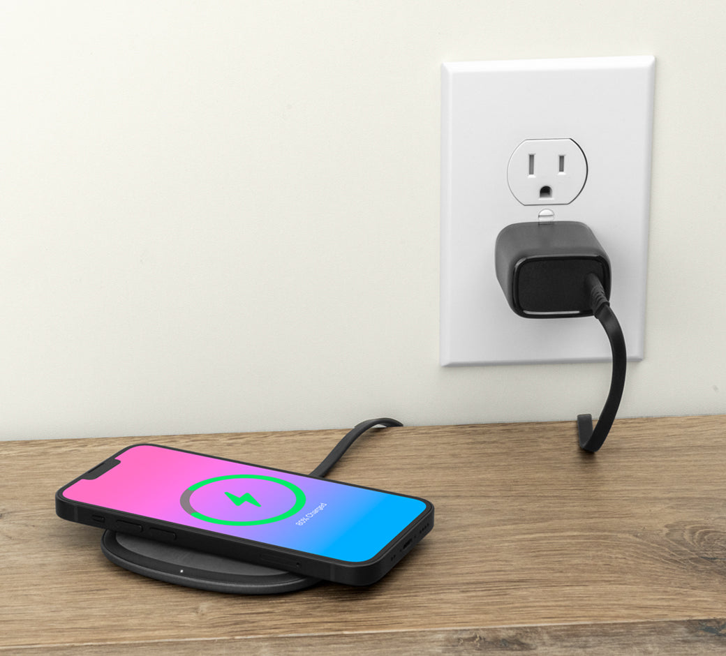 A smartphone charging on a wireless pad connected to a wall outlet via a black adapter on a wooden surface.