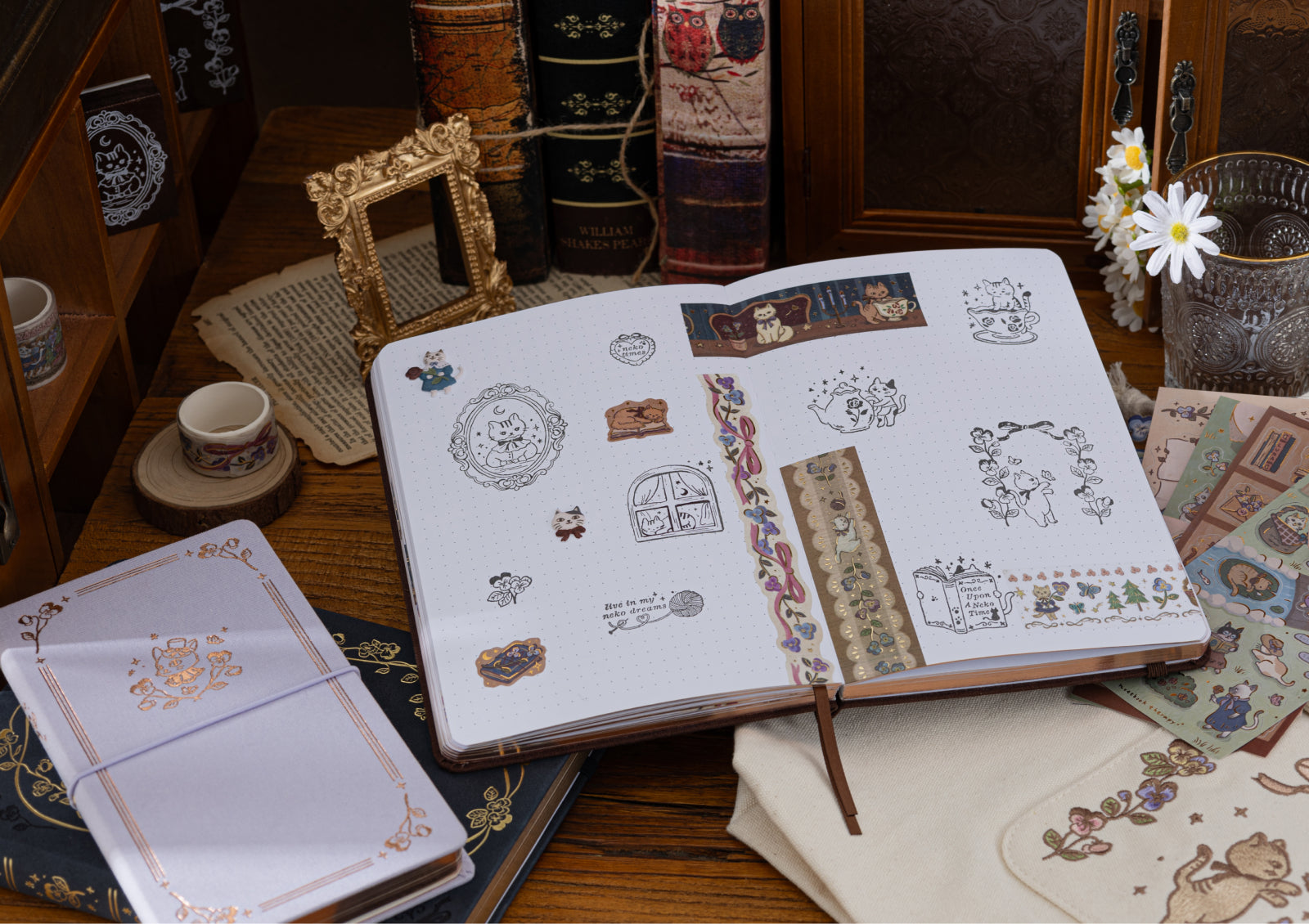 A lifestyle scene on a wooden desk showing a journal decorated with cat stamps and washi tape, surrounded by other stationery items and books.