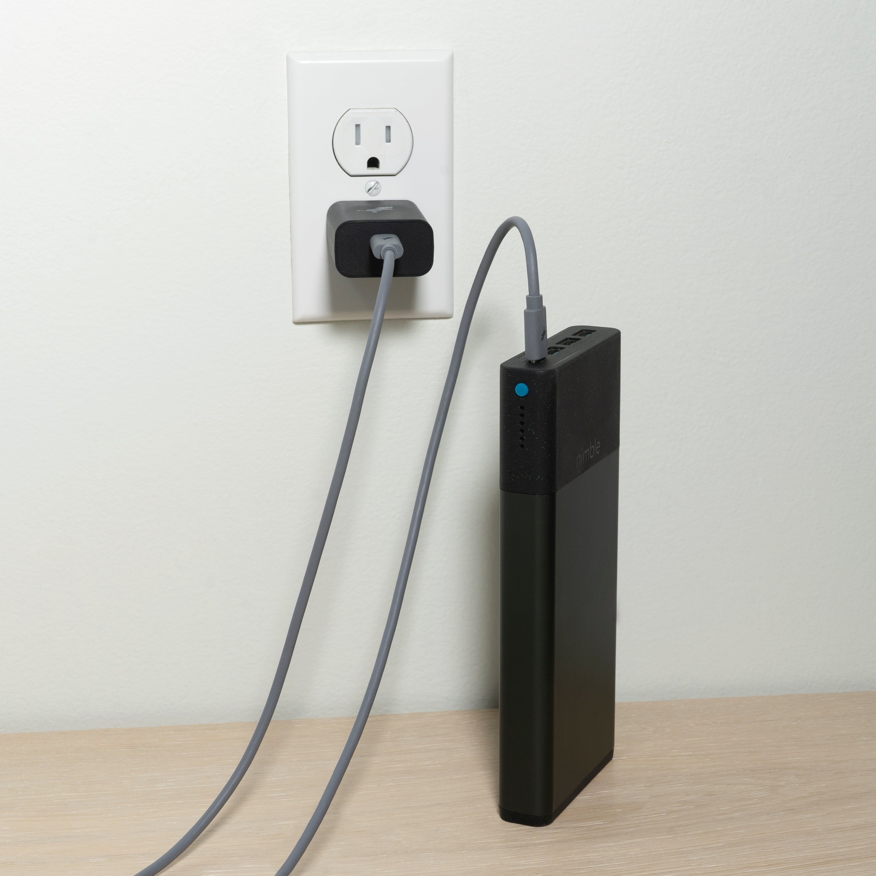 Black power bank plugged into a wall outlet with a grey adapter.
