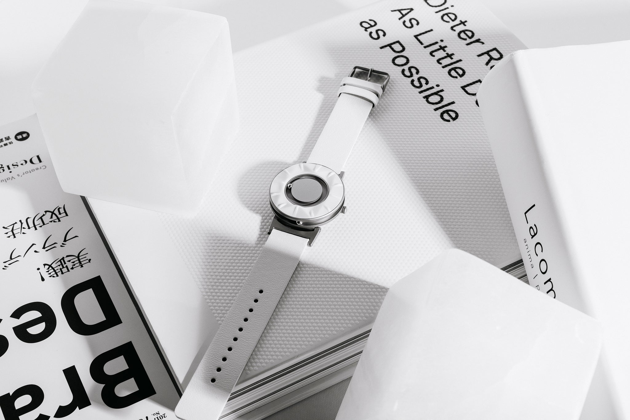 The Bradley Element White rests on a white book. It is surrounded by various white objects. There is a shadow cast over part of the strap.