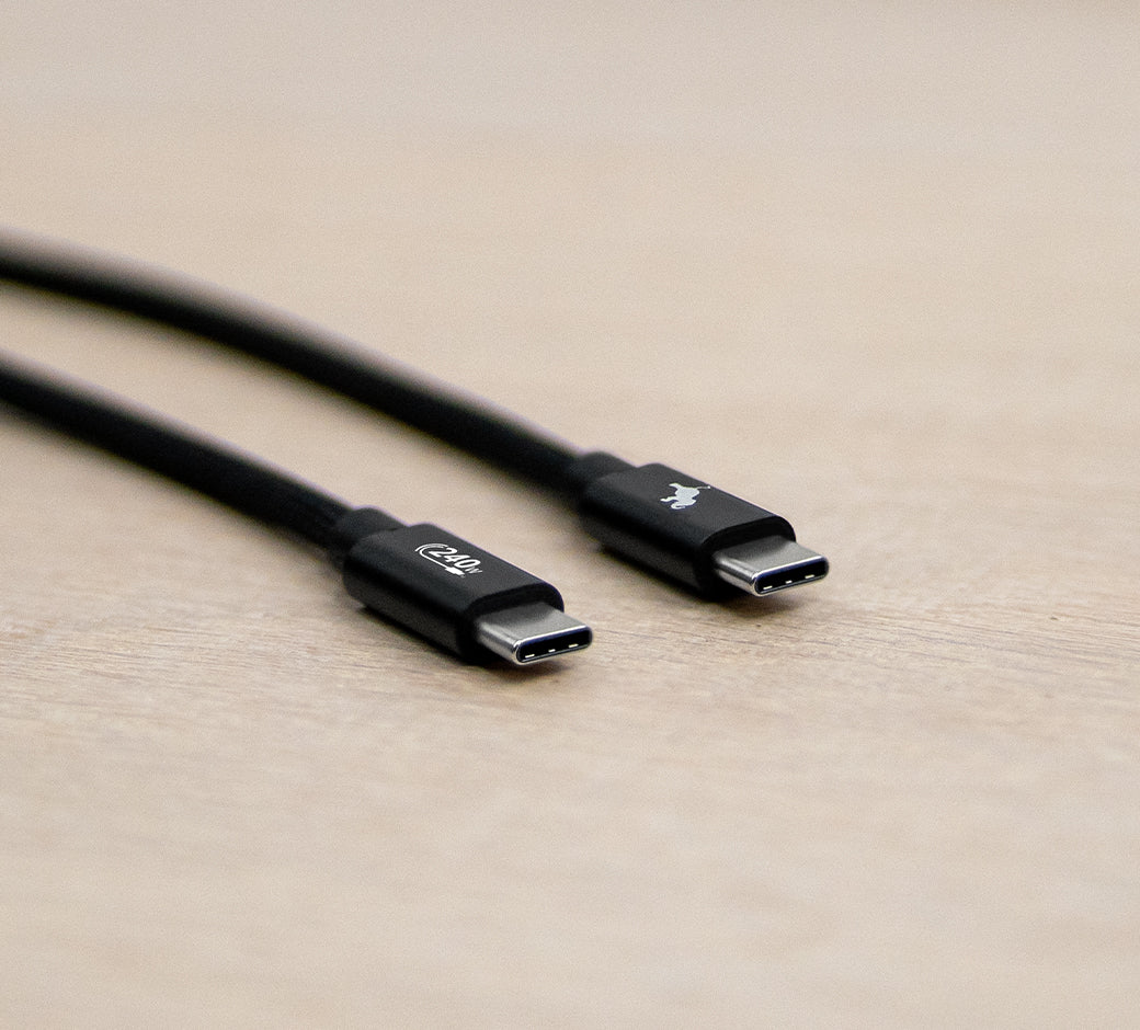 Close-up of two black USB-C cable connectors on a light wooden surface.
