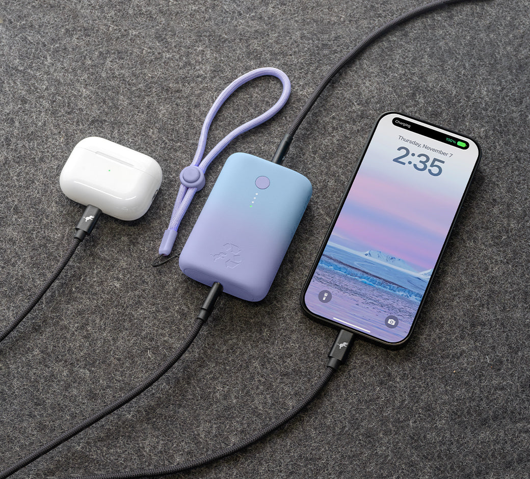 Portable charger connected to a smartphone and wireless earbuds case on a gray surface.