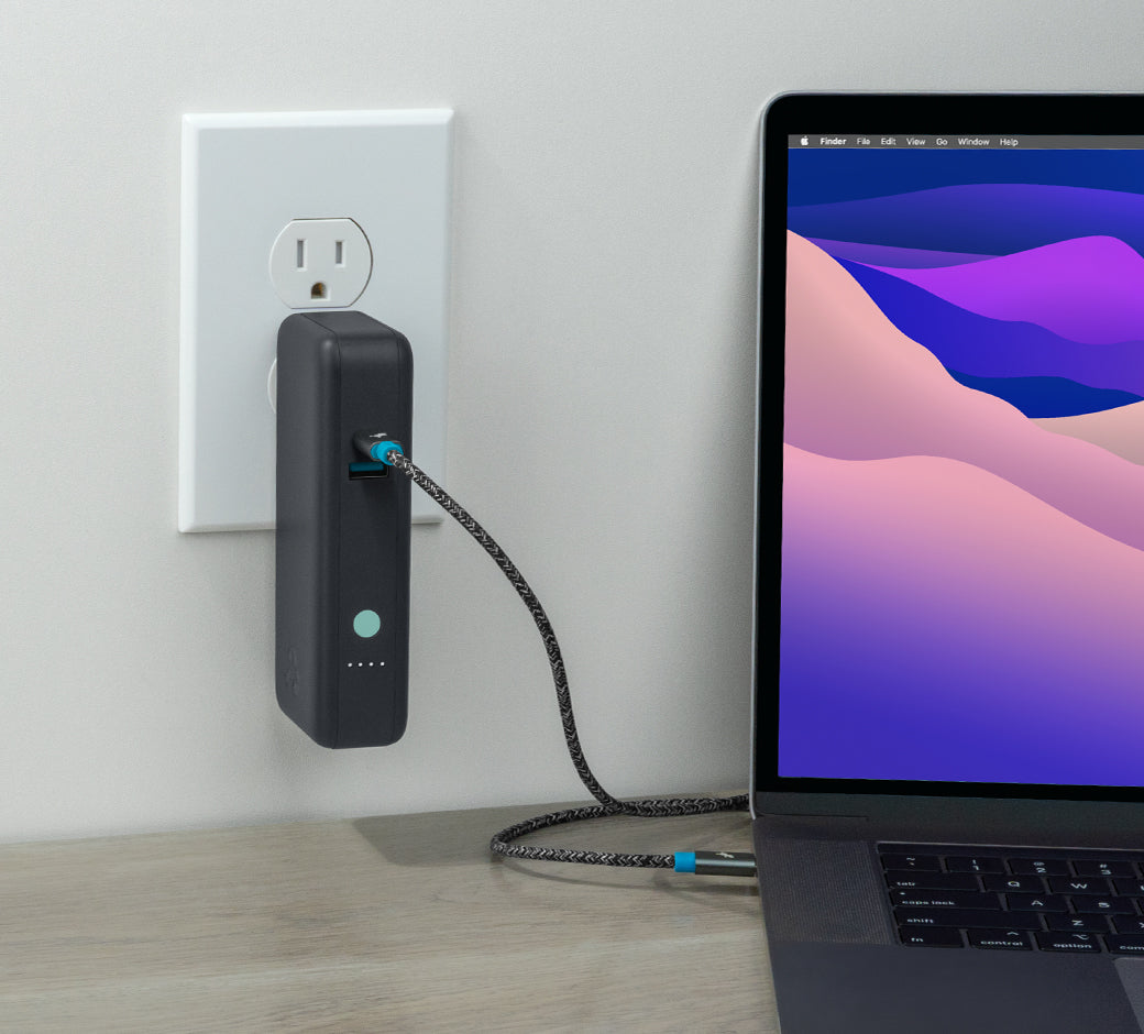 Power bank connected to a wall outlet, charging a laptop on a desk.