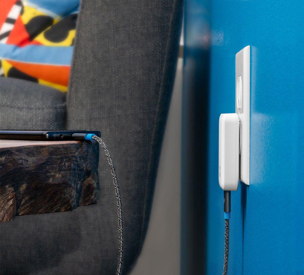 Slim wall charger plugged in, charging a device on a rustic wooden table.