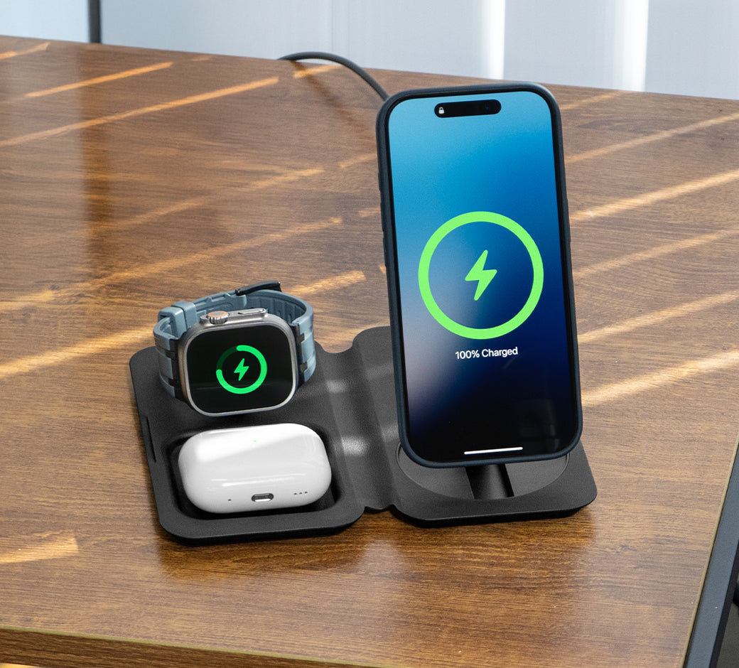 A phone and Apple Watch on a charging stand with a 100% charge displayed on the phone.