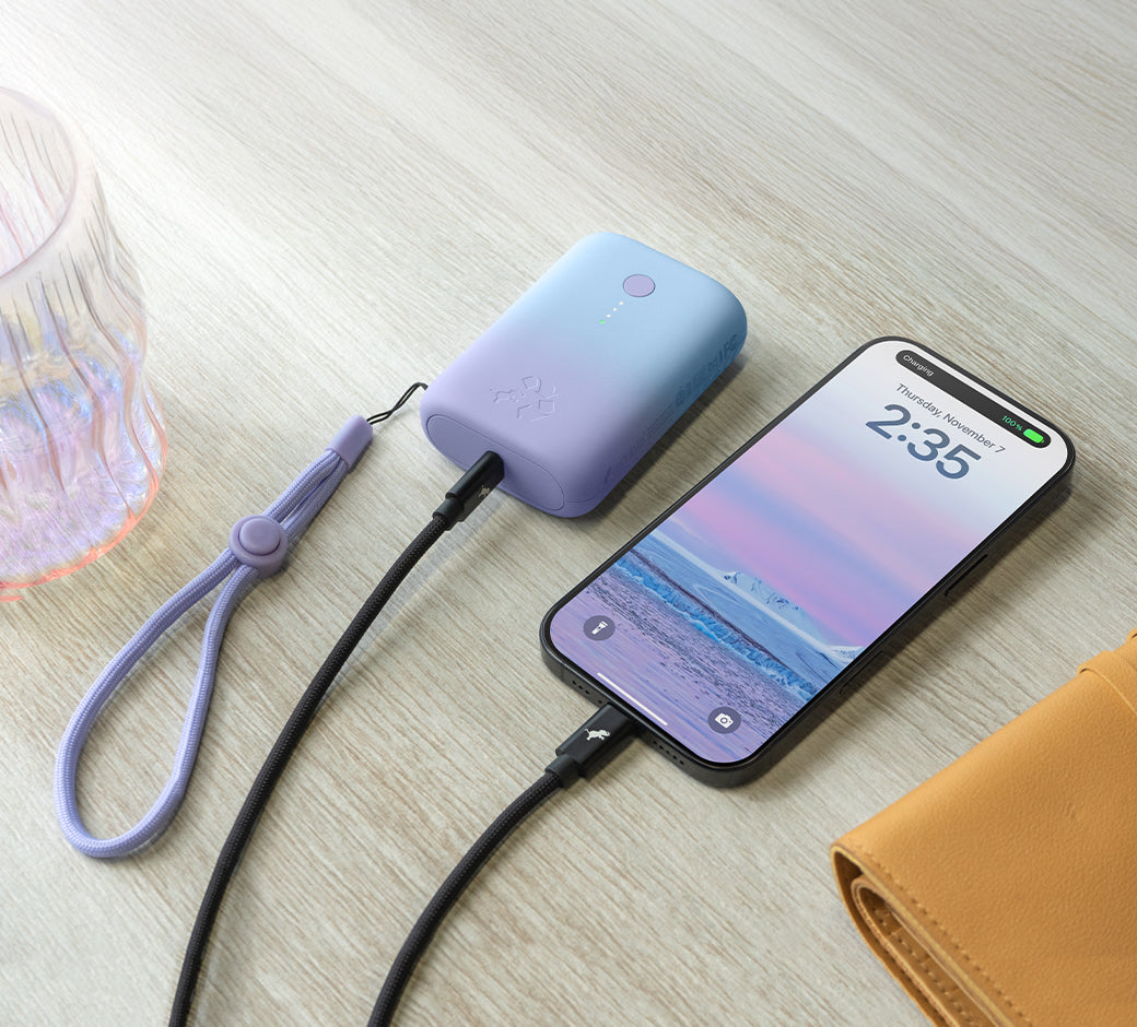 Portable battery charging a smartphone on a table next to a glass and wallet.