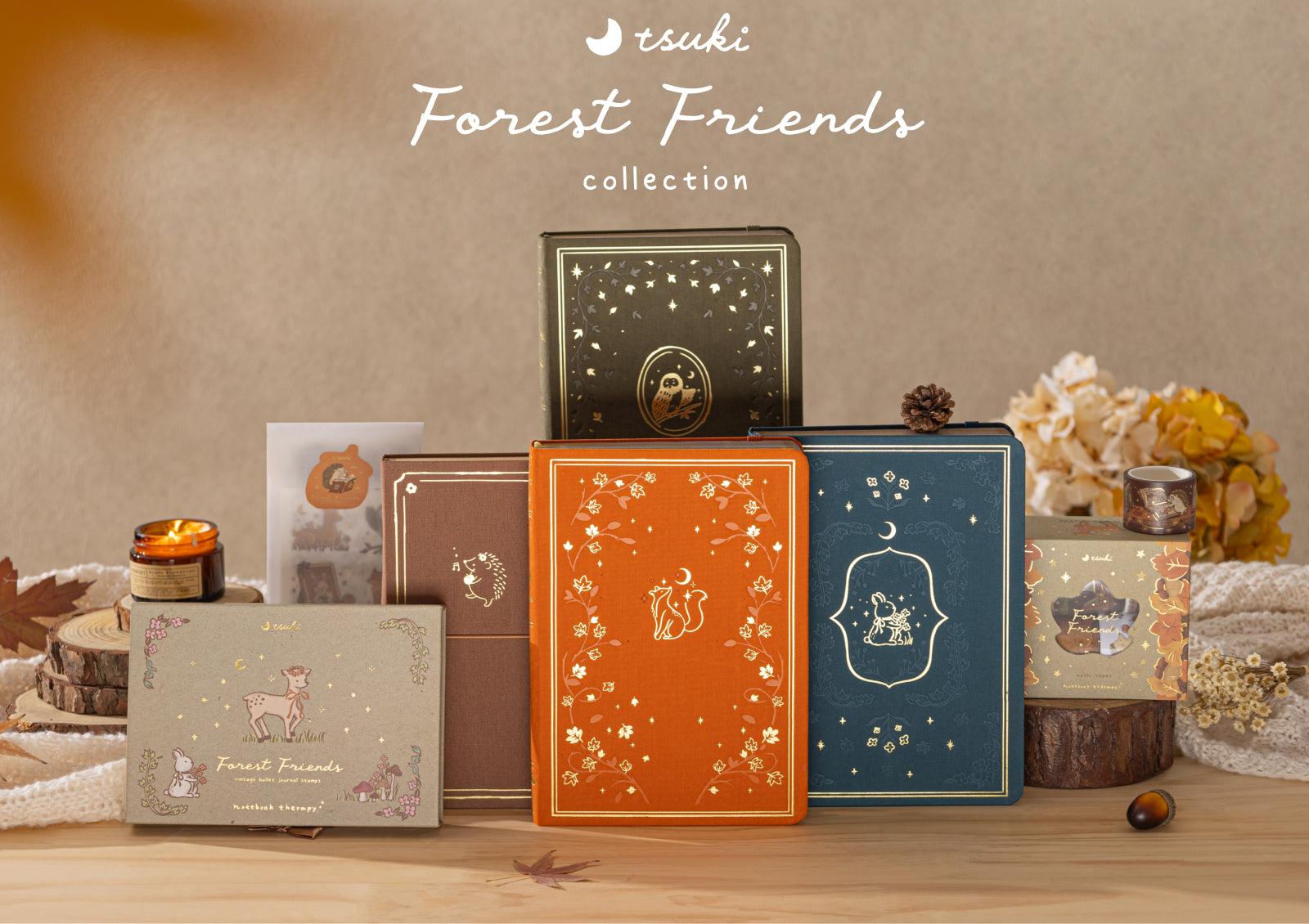 Styled display of the Tsuki Forest Friends collection featuring four notebooks, stamp box, washi tapes, stickers, and autumn decor with the Forest Friends logo.